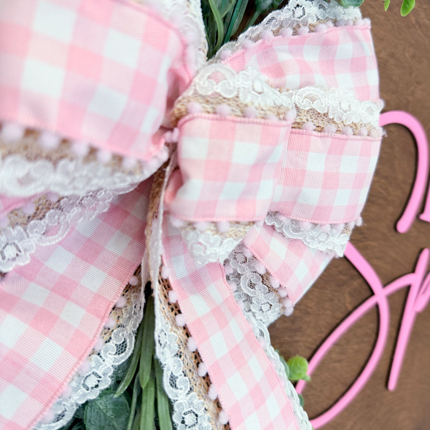 Close-up of a pink checkered bow with lace details on a wooden surface.