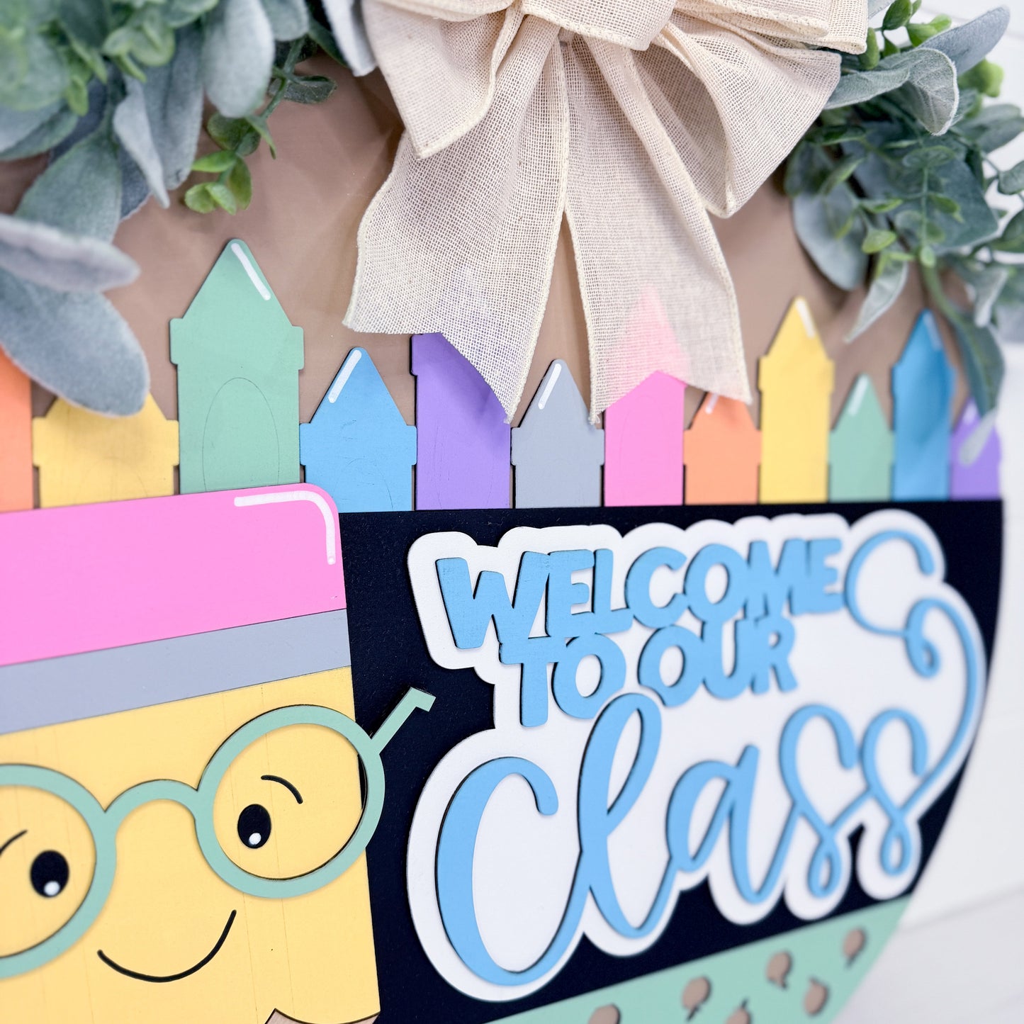 Decorative wreath with colorful crayons, a smiling face, and 'Welcome to our Class' text.