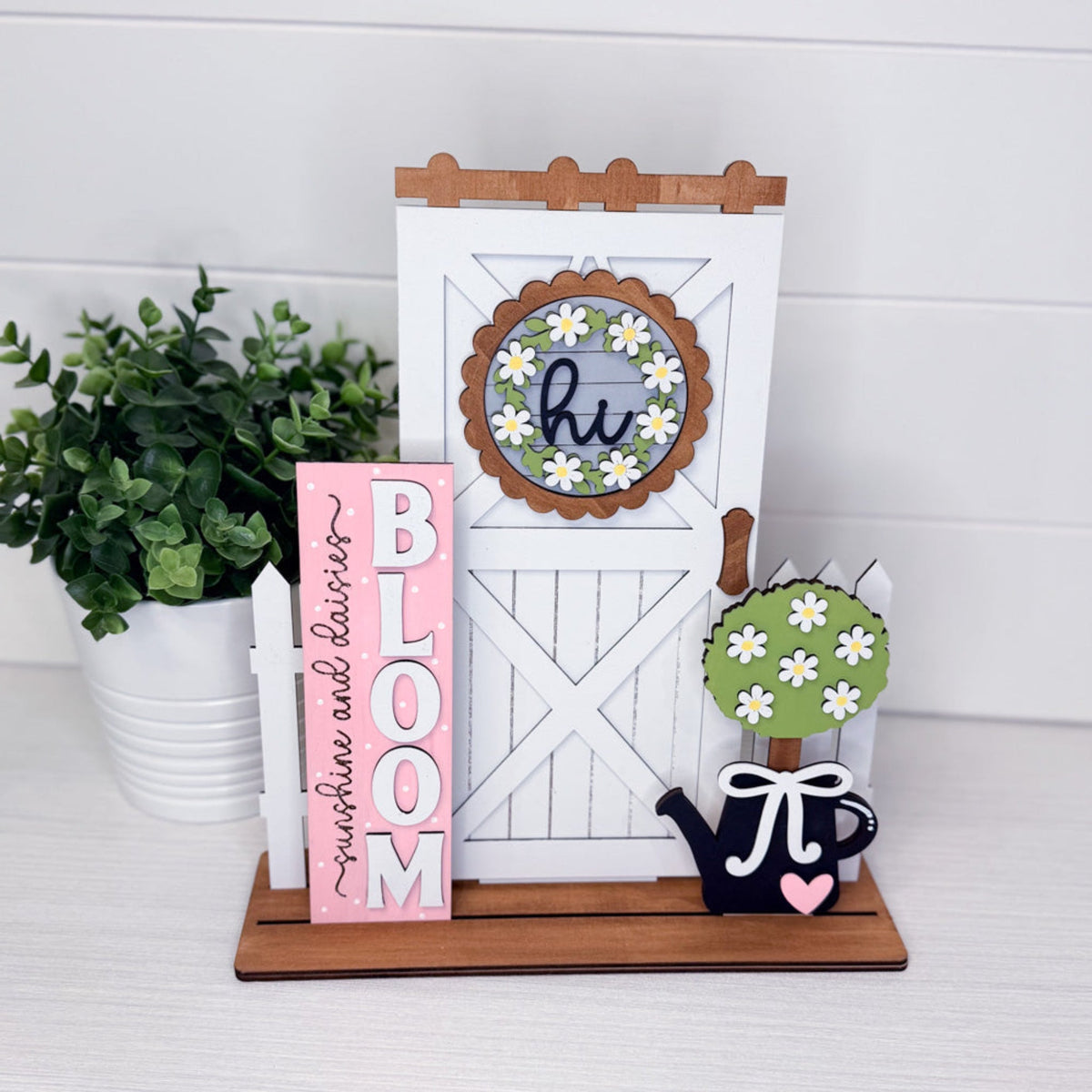 Decorative items including a pink 'BLOOM' sign, white board with wooden frame, and small plant on a white surface.