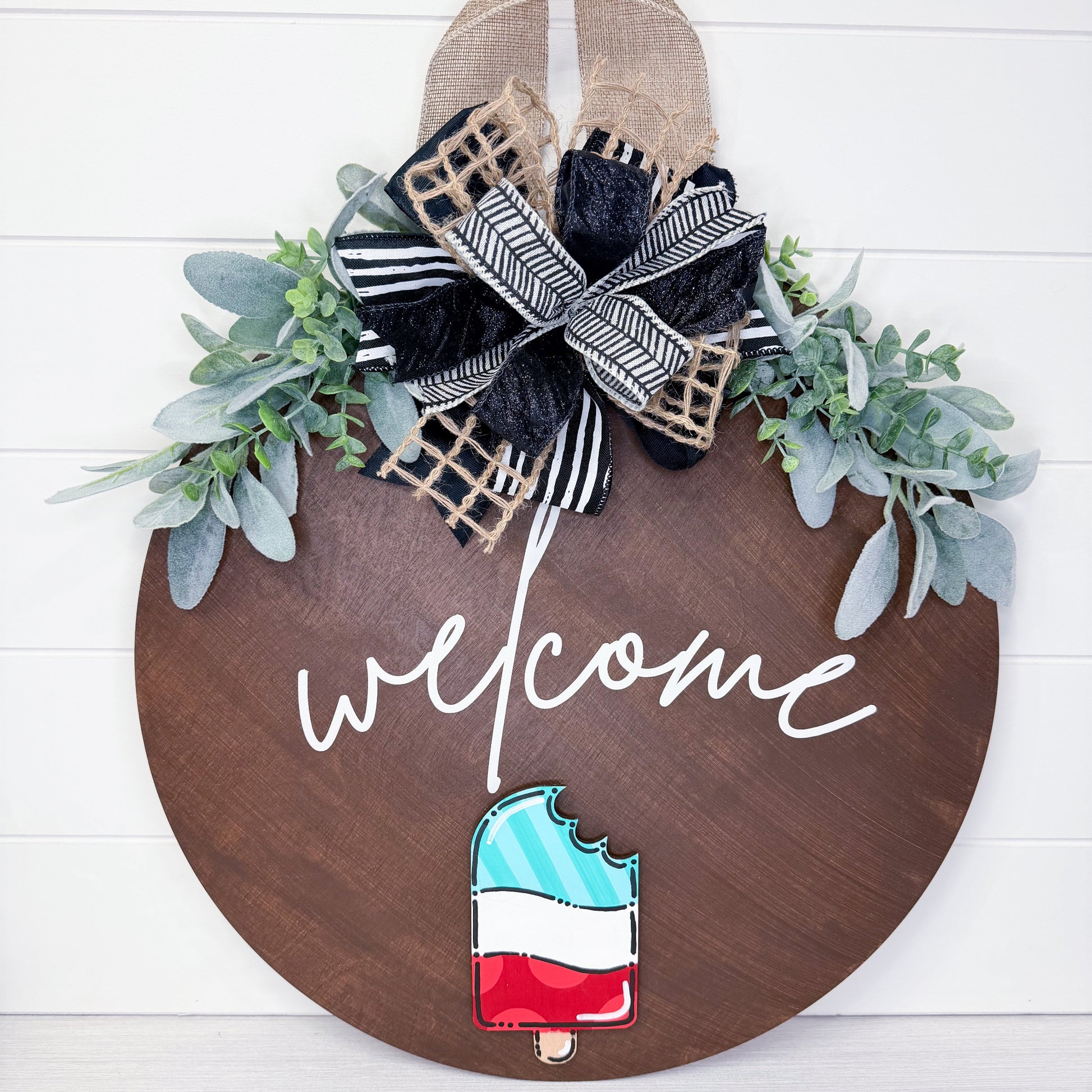 Decorative wooden sign with 'welcome' text, floral elements, and a popsicle design on a white background.
