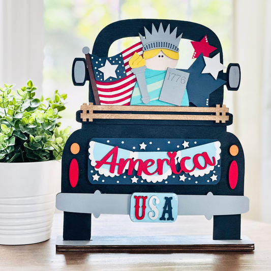 A decorative wooden truck with interchangeable insert featuring American patriotic colors and symbols, such as the Statue of Liberty and the American flag.