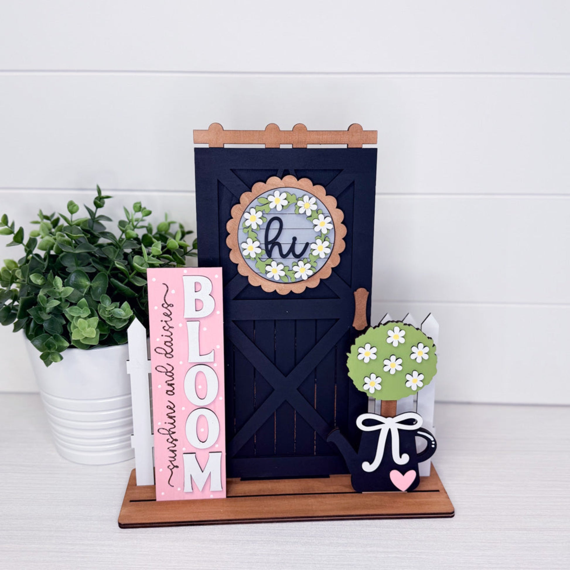 Decorative items including a black door, pink sign, and small tree with flowers on a white surface.