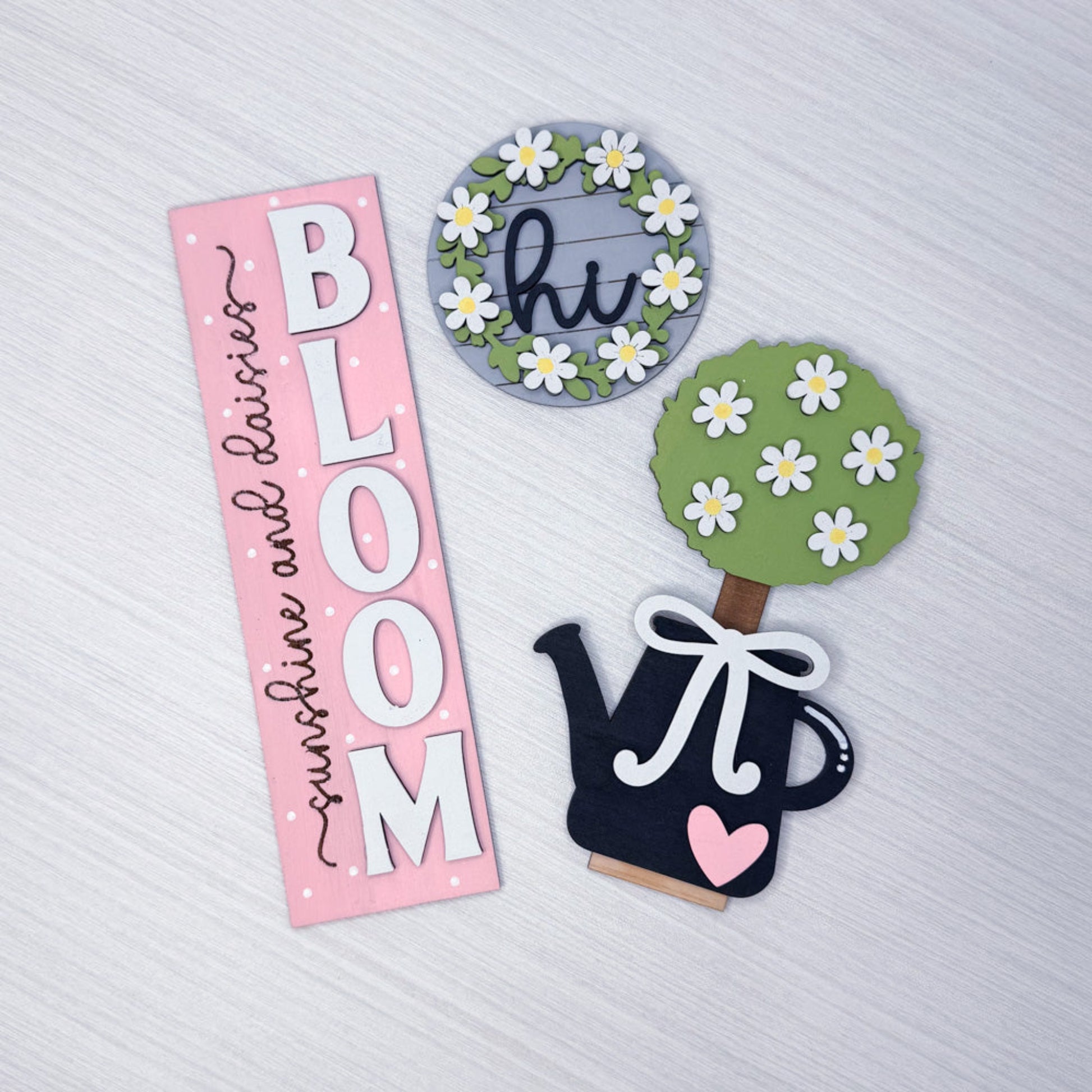 Decorative elements including a pink sign with 'BLOOM', a tree with flowers, and a watering can on a textured white background.