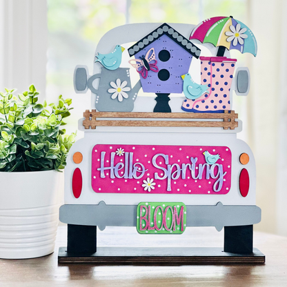 A decorative wood insert featuring a vintage truck with a birdhouse on the back, displaying the text 'Hello Spring' and various floral and polka dot patterns.