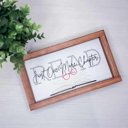 Decorative sign with 'READ' and 'Just One More Chapter' text in a wooden frame on a light background.