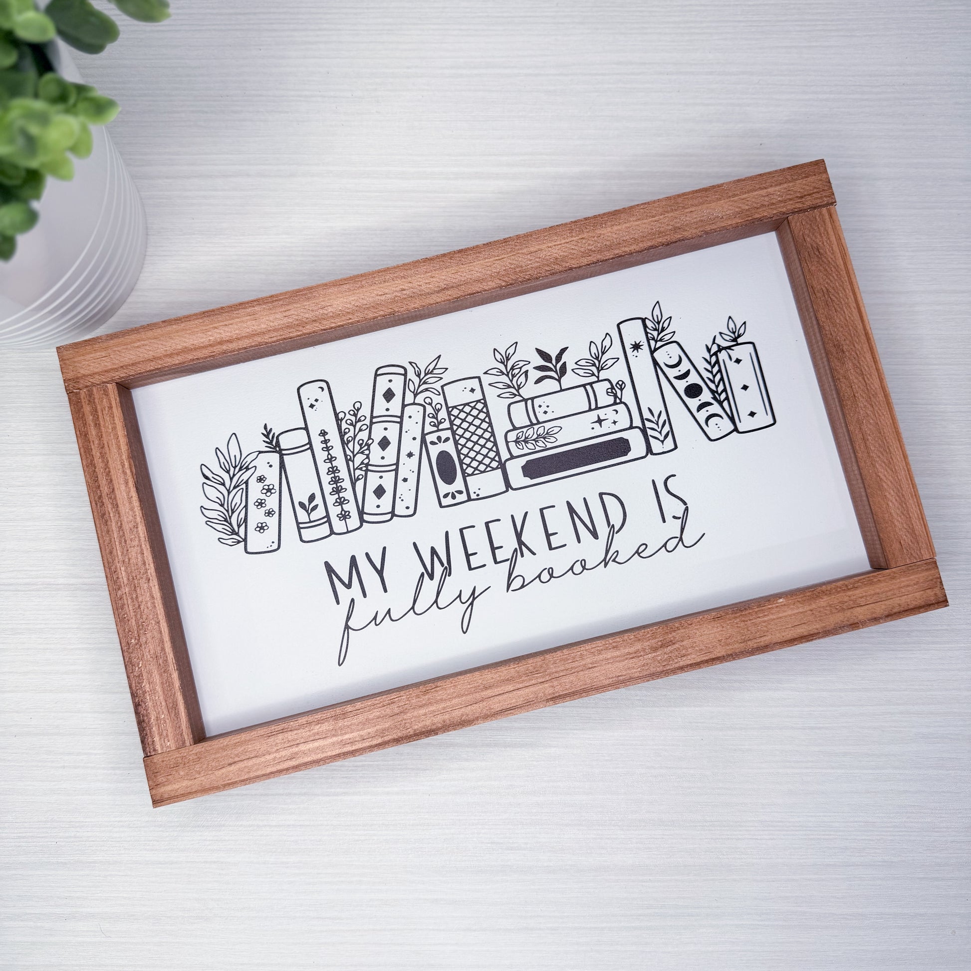 Wooden-framed sign with 'My weekend is fully booked' text and book illustrations on a white background.