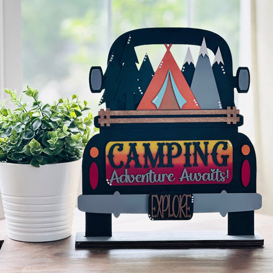 Decorative sign of a camper van with camping-themed text on a wooden surface.
