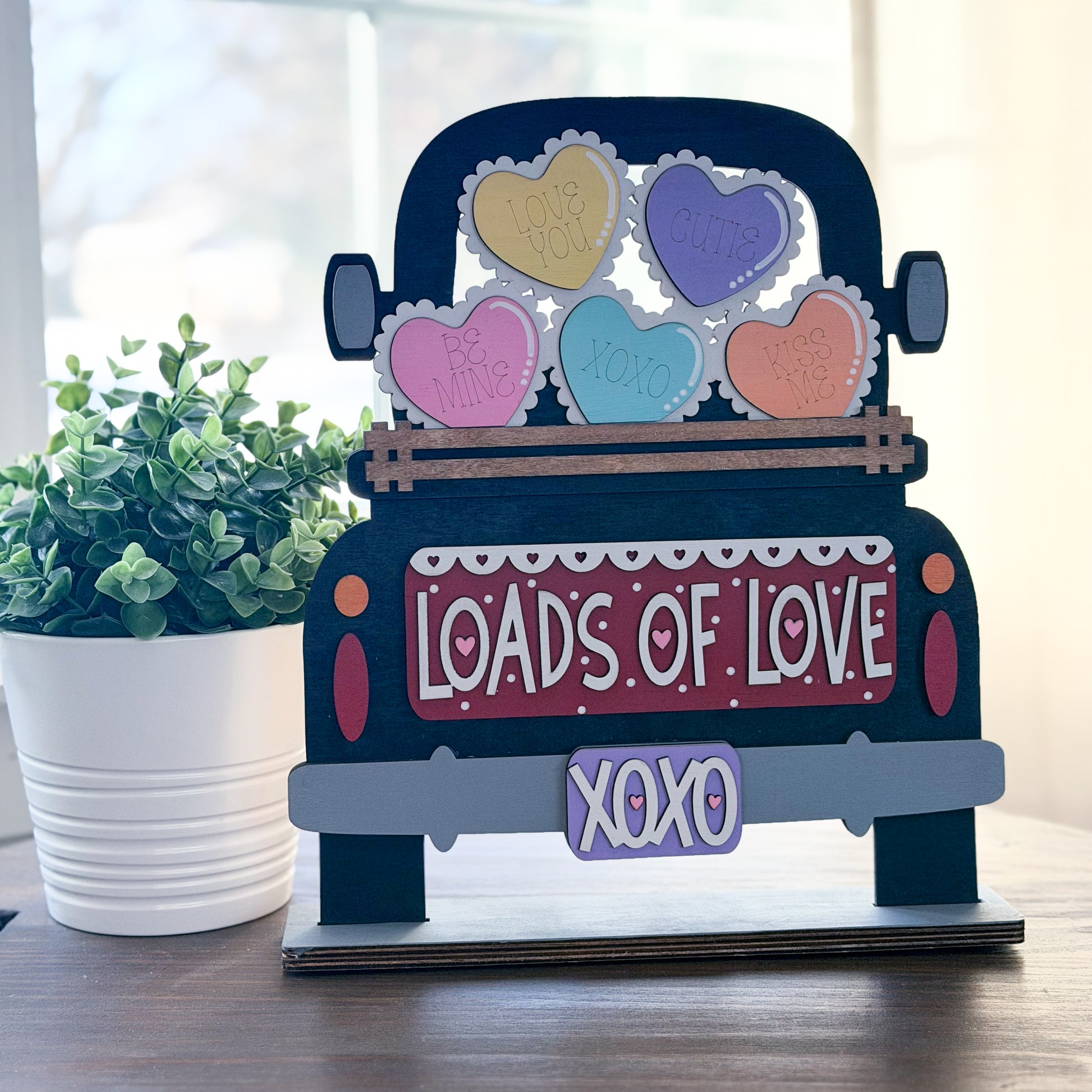 Decorative sign shaped like a truck with heart-shaped candies and 'Loads of Love' text on a wooden surface.