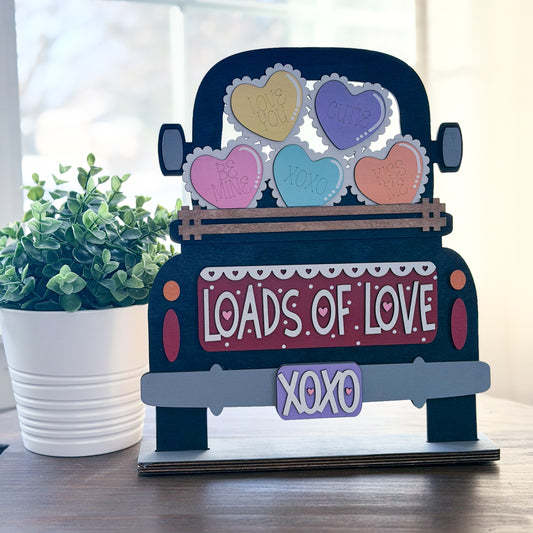 Decorative sign shaped like a truck with heart-shaped candies and 'Loads of Love' text on a wooden surface.