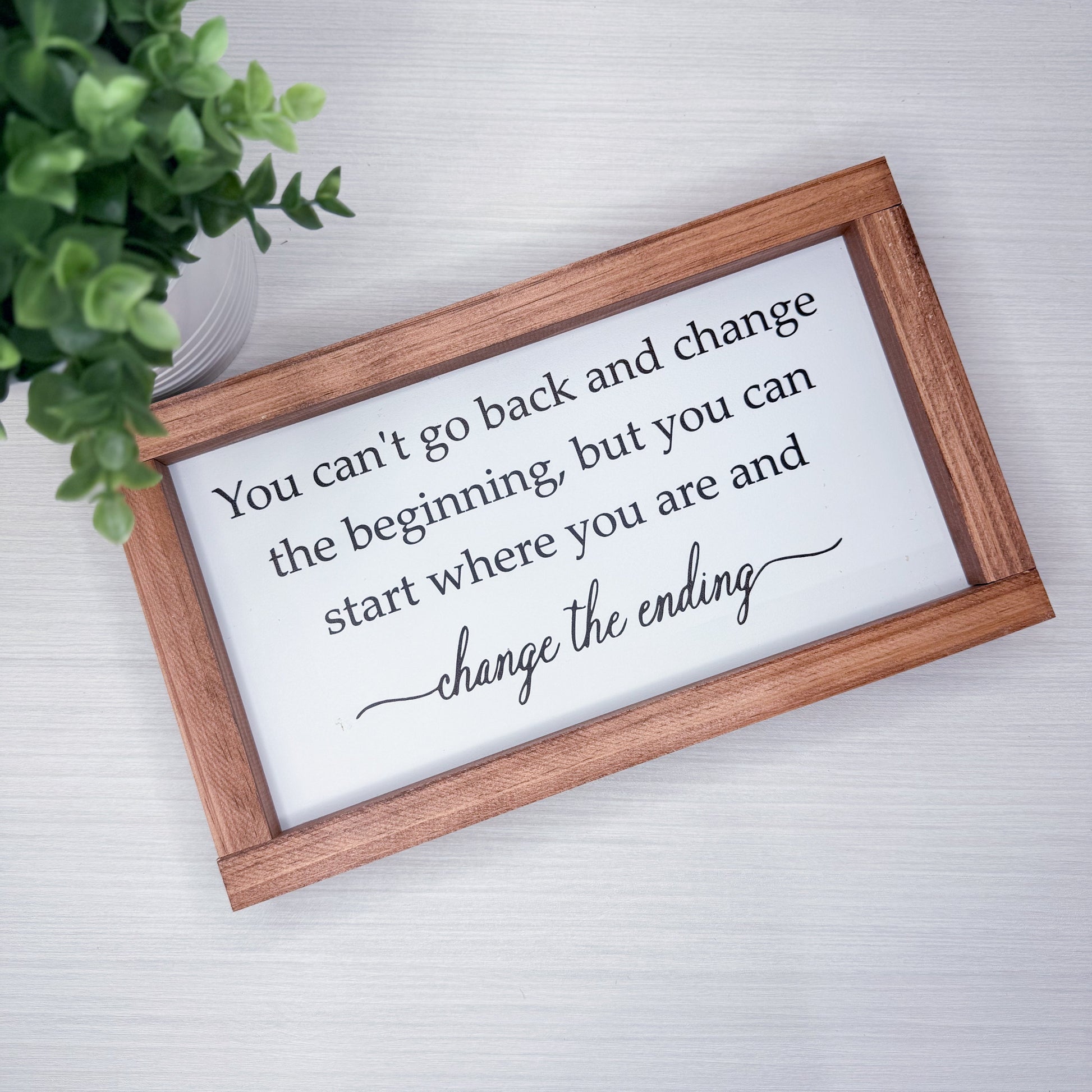 Wooden-framed sign with motivational quote on a light background