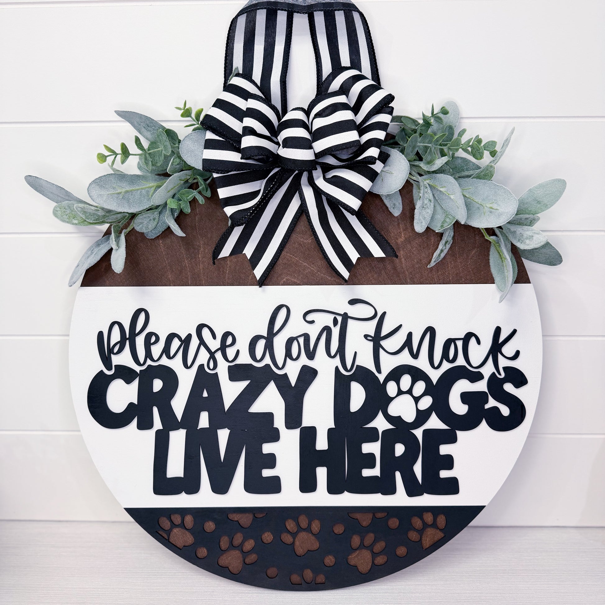 Decorative sign with text 'Please don't knock crazy dogs live here' and a bow on a white background