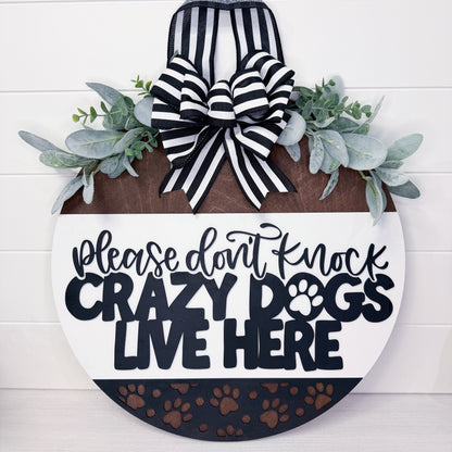 Decorative sign with text 'Please don't knock crazy dogs live here' and a bow on a white background