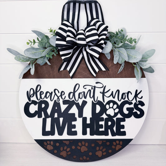Decorative sign with text 'Please don't knock crazy dogs live here' and a bow on a white background