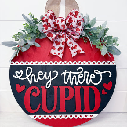 Decorative sign with a heart shape, bow, and 'hey there Cupid' text on a white background
