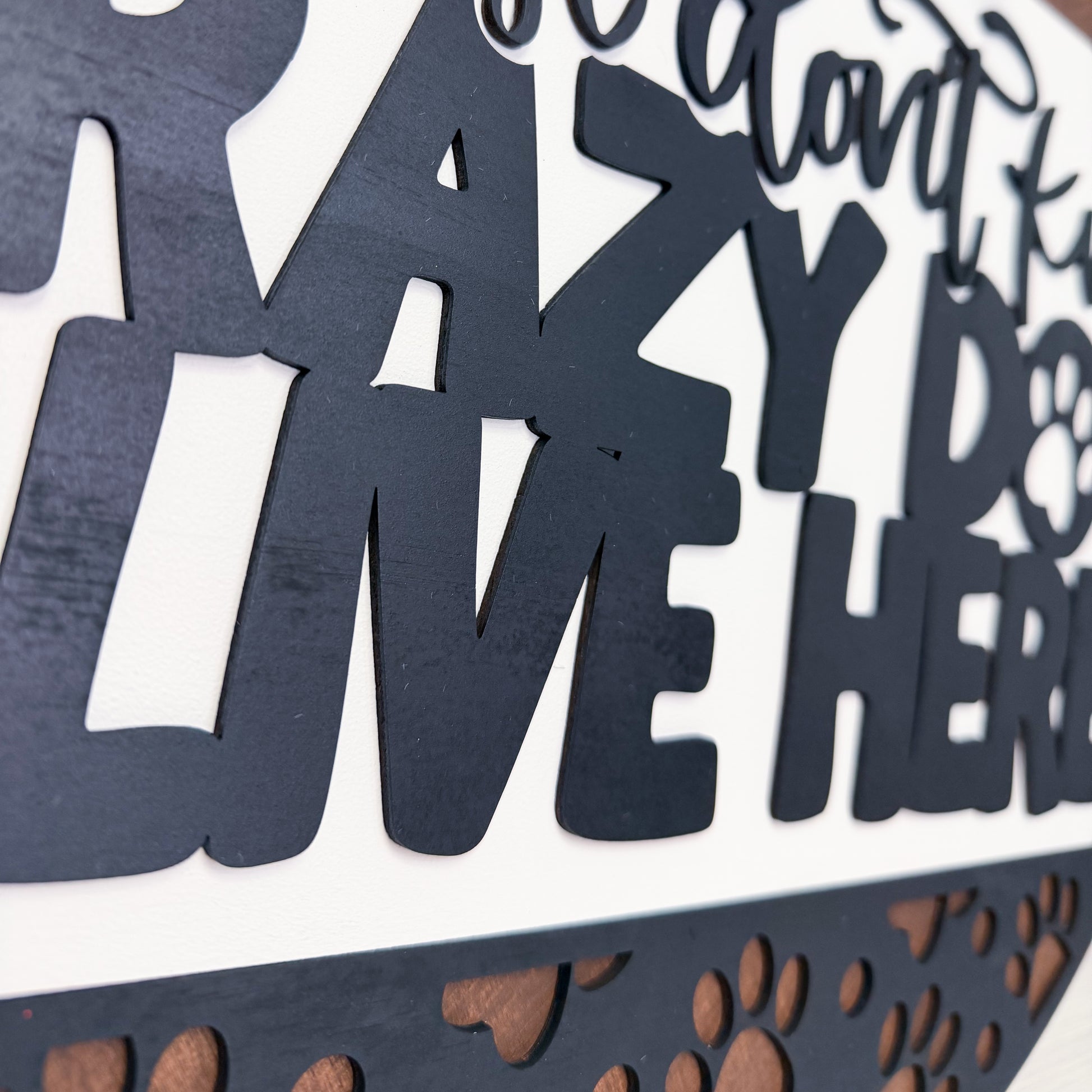 Black cut-out letters spelling 'LIVE HERE' with paw prints on a white background