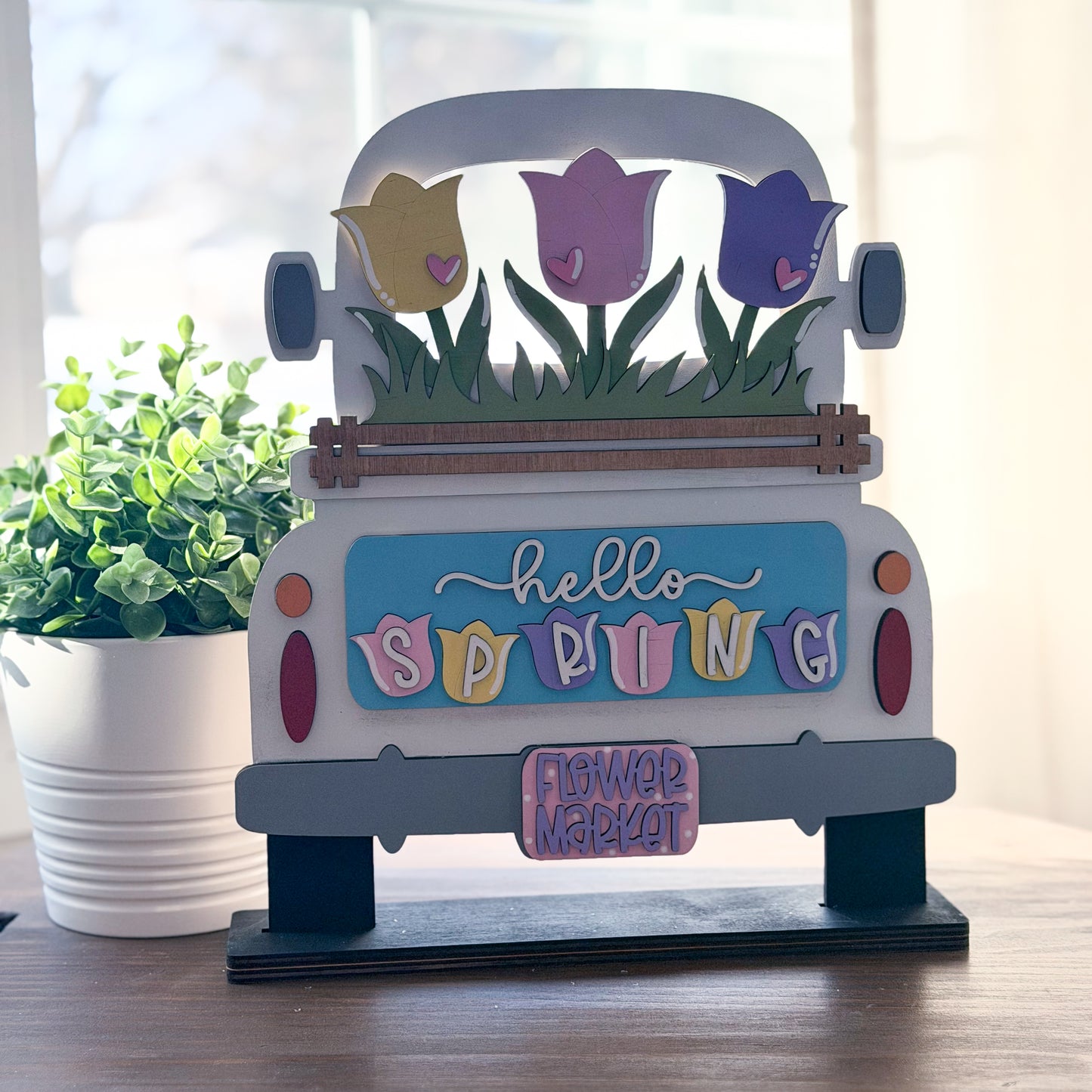 Decorative sign shaped like a truck with spring-themed elements on a wooden surface.