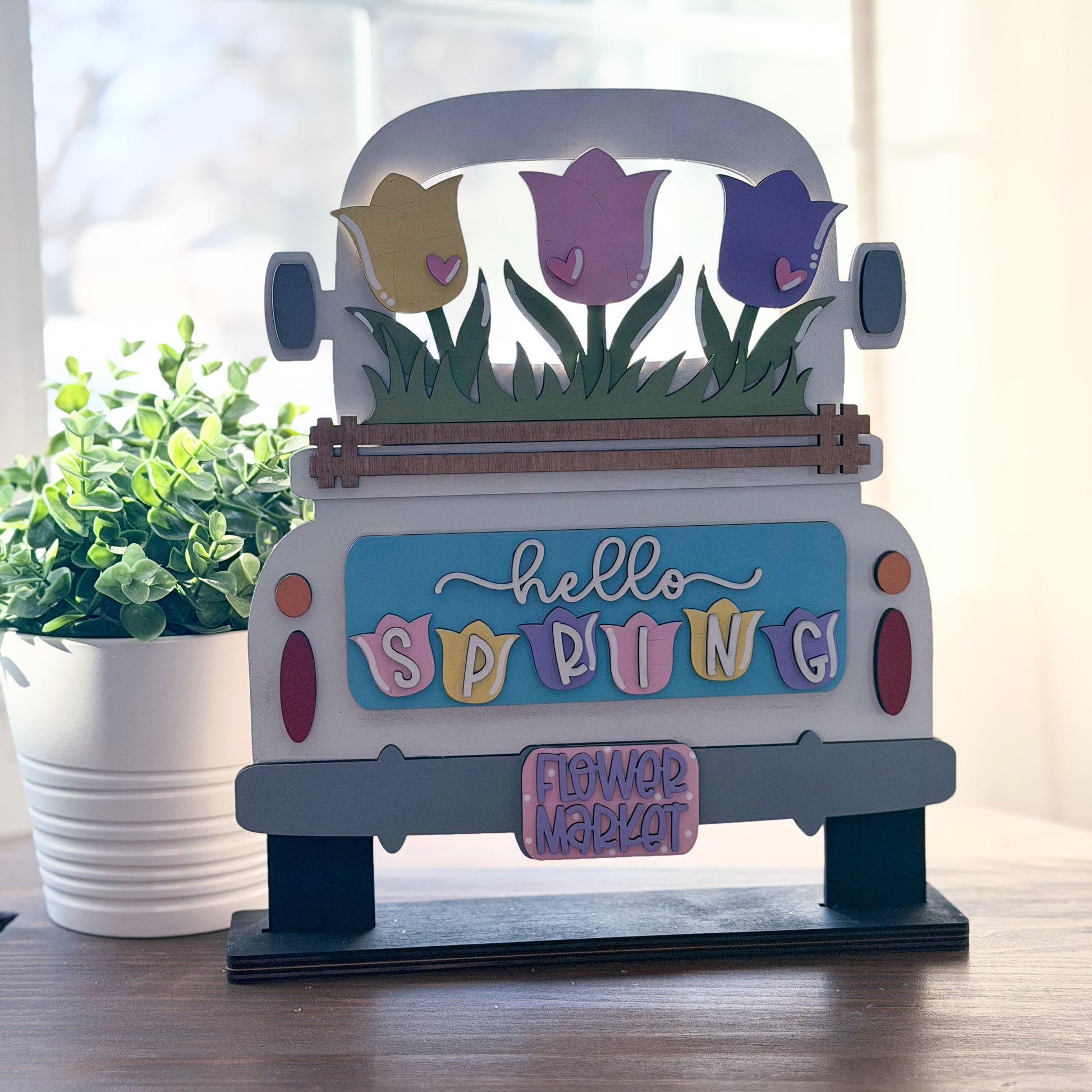 Decorative sign shaped like a truck with spring-themed elements on a wooden surface.
