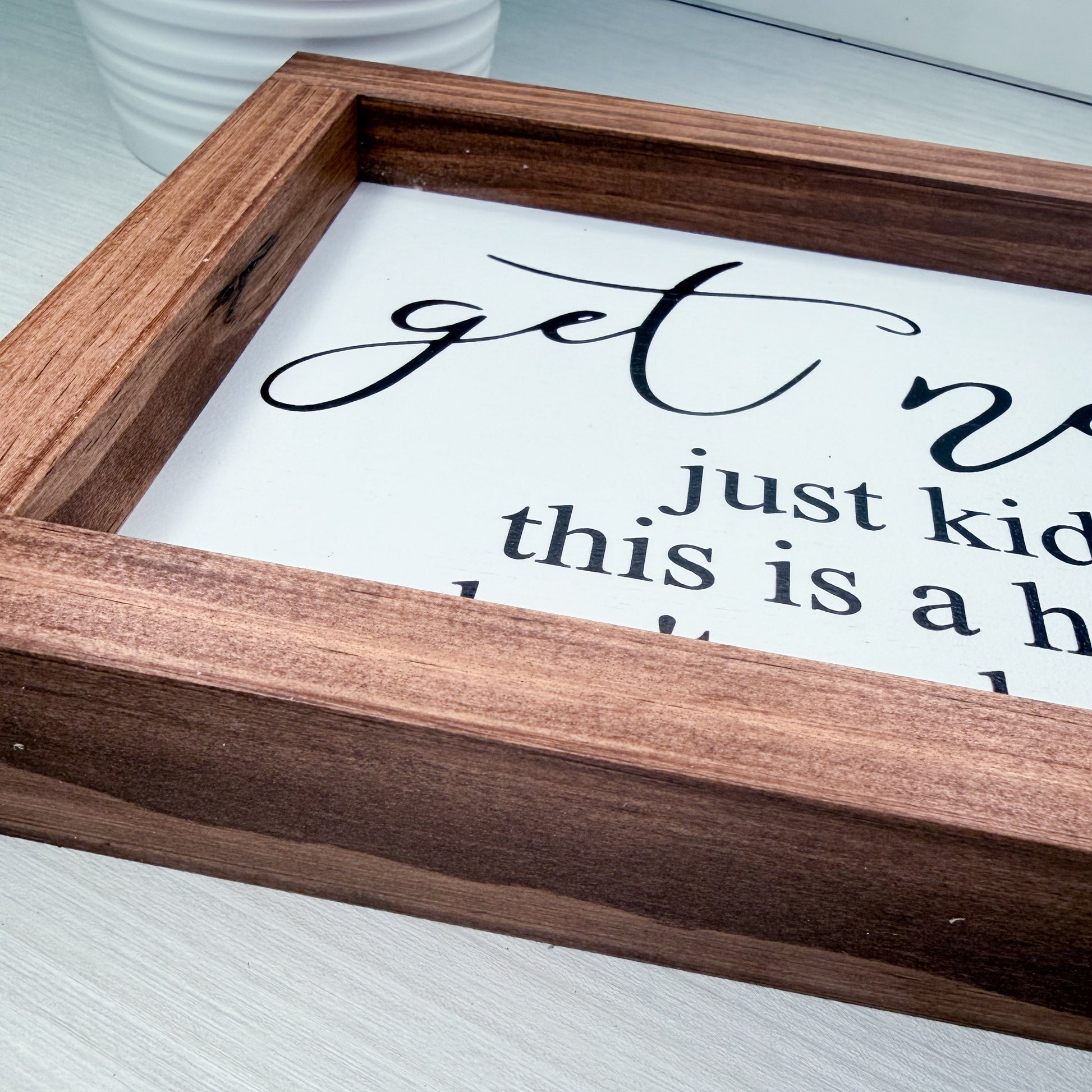Wooden-framed sign with humorous text on a white surface