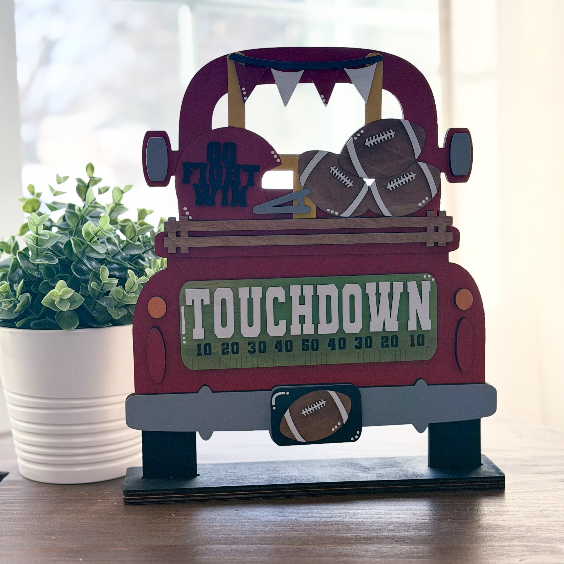 Decorative wooden truck with football-themed items on a table next to a plant.
