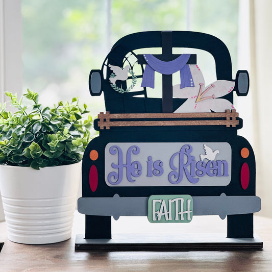 Decorative sign shaped like a truck with 'He is Risen' and 'Faith' text on a table.