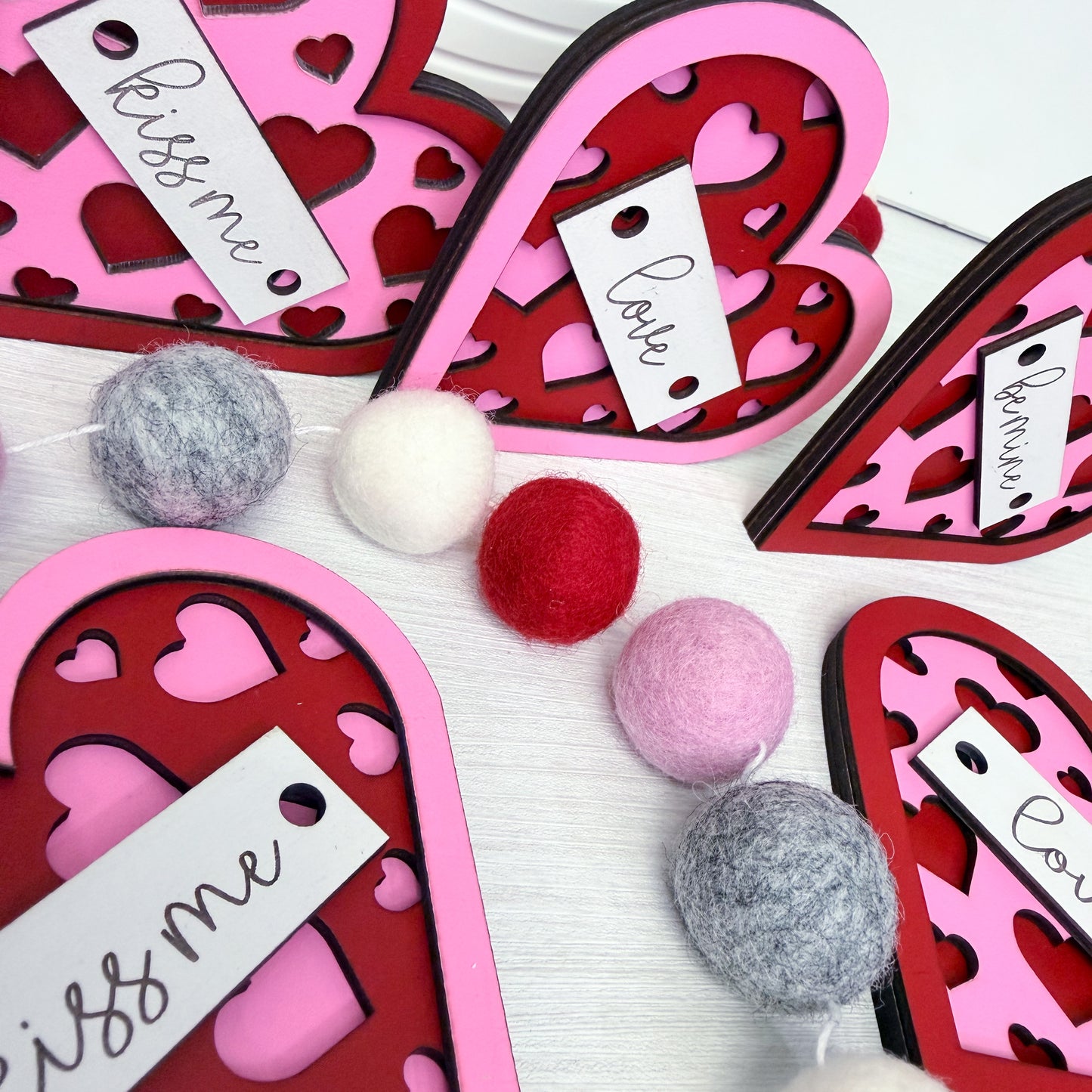 Heart-shaped pink and red card holders with pom-poms on a white background