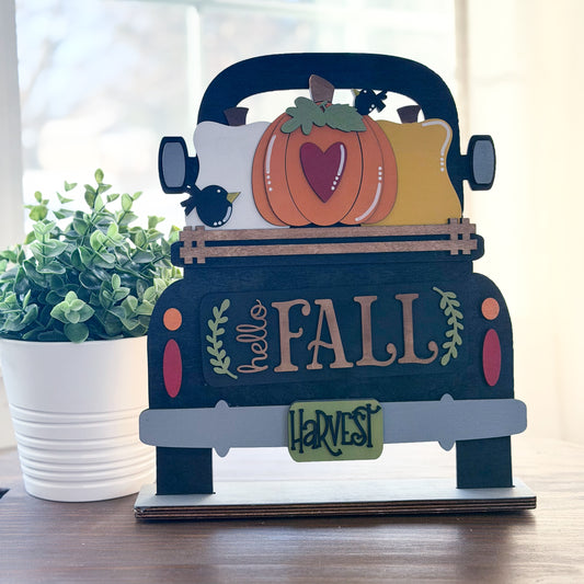 Decorative sign with 'hello FALL' and pumpkins on a truck, placed indoors.