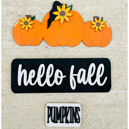 A decorative wood truck with 'hello fall' and 'pumpkin' text, carrying pumpkins on its bed, placed on a table.