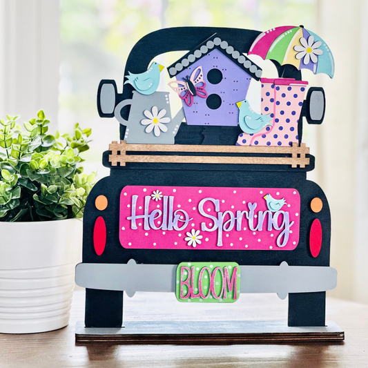 A decorative wood insert featuring a vintage truck with a birdhouse on the back, displaying the text 'Hello Spring' and various floral and polka dot patterns.