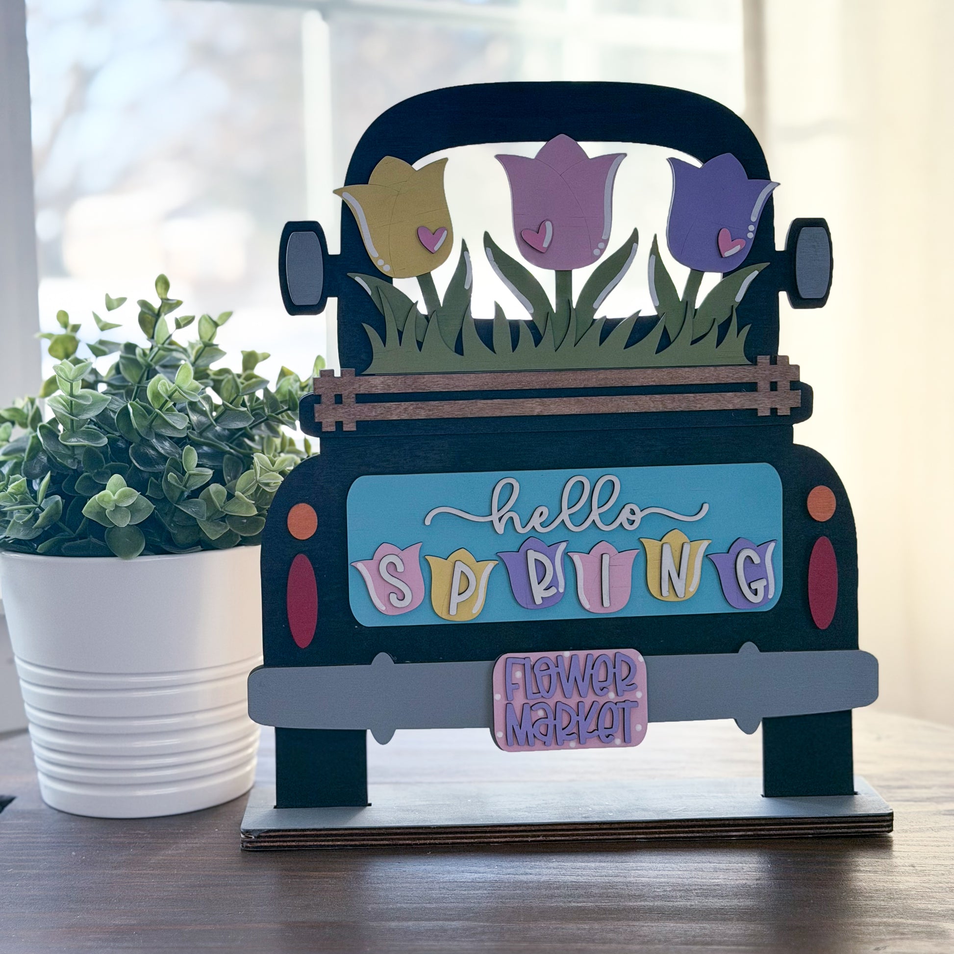 Decorative sign shaped like a truck with spring flowers and 'hello spring' text on a wooden surface.