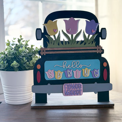 Decorative sign shaped like a truck with spring flowers and 'hello spring' text on a wooden surface.