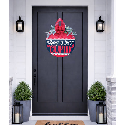 Decorative door hanger with 'Hey There Cupid' text on a black door.