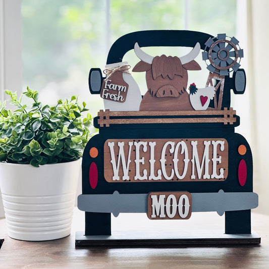 Decorative sign of a truck with a cow and 'Welcome Moo' text on a wooden surface.
