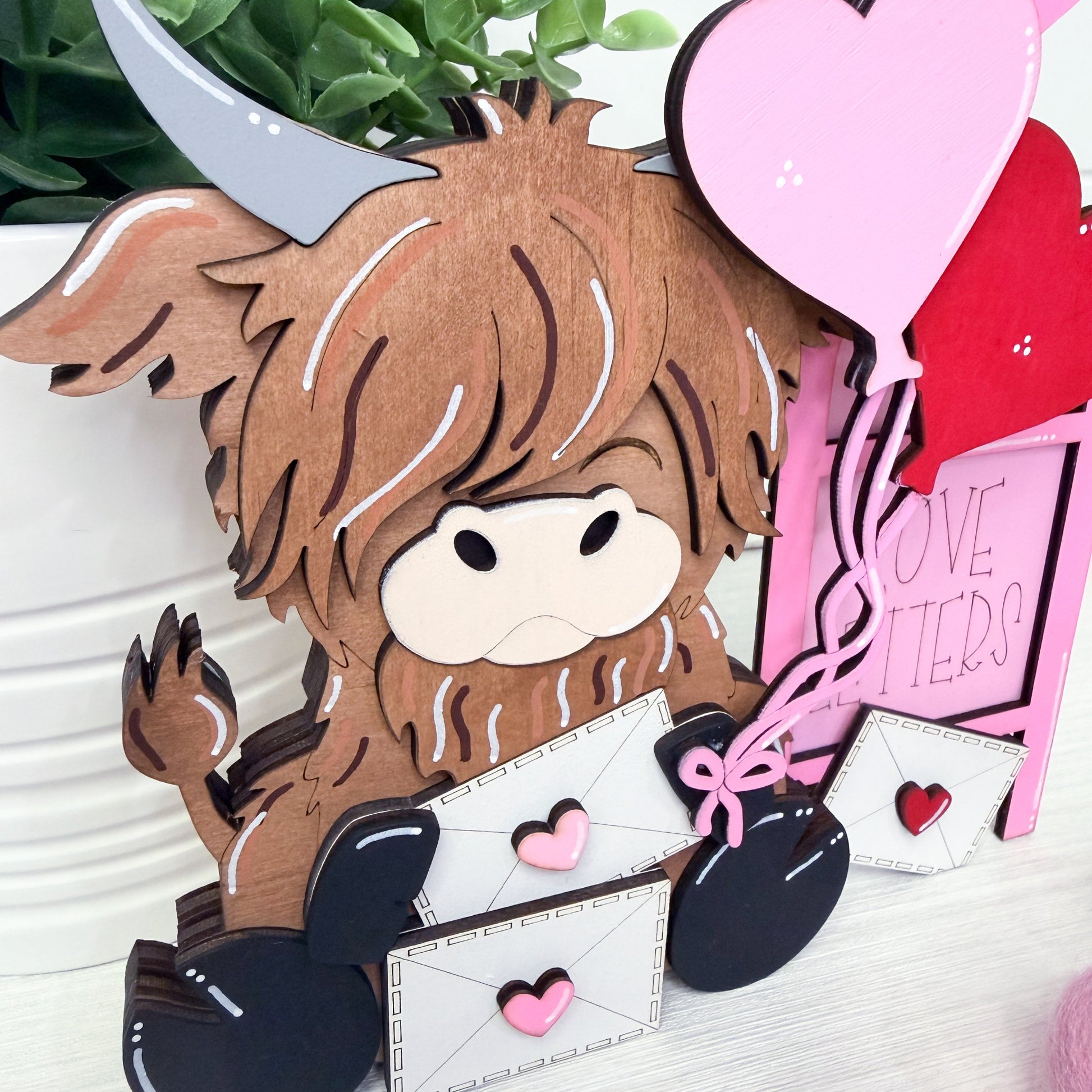 Wooden cow figurine with heart-shaped balloons and letters on a white surface