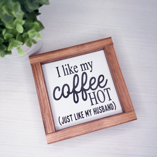 Wooden-framed sign with humorous text on a white surface with a plant in the corner.