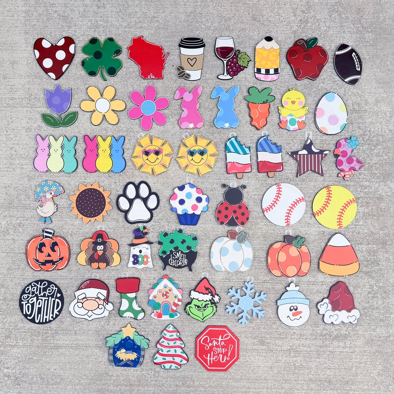 A flat lay of 40 colorful wooden pieces The pieces feature various autumn and holiday designs including pumpkins, candy corn, snowman, Santa Claus, Christmas tree, paw print, and fall leaves.