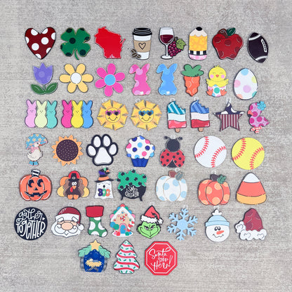 A flat lay of 40 colorful wooden pieces The pieces feature various autumn and holiday designs including pumpkins, candy corn, snowman, Santa Claus, Christmas tree, paw print, and fall leaves.