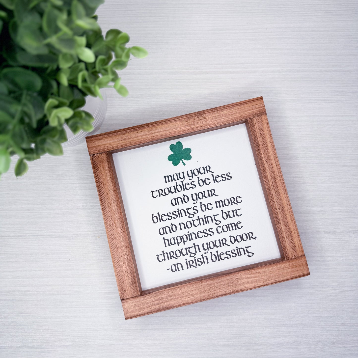 Wooden-framed print with inspirational quote and green clover on a light gray wall.