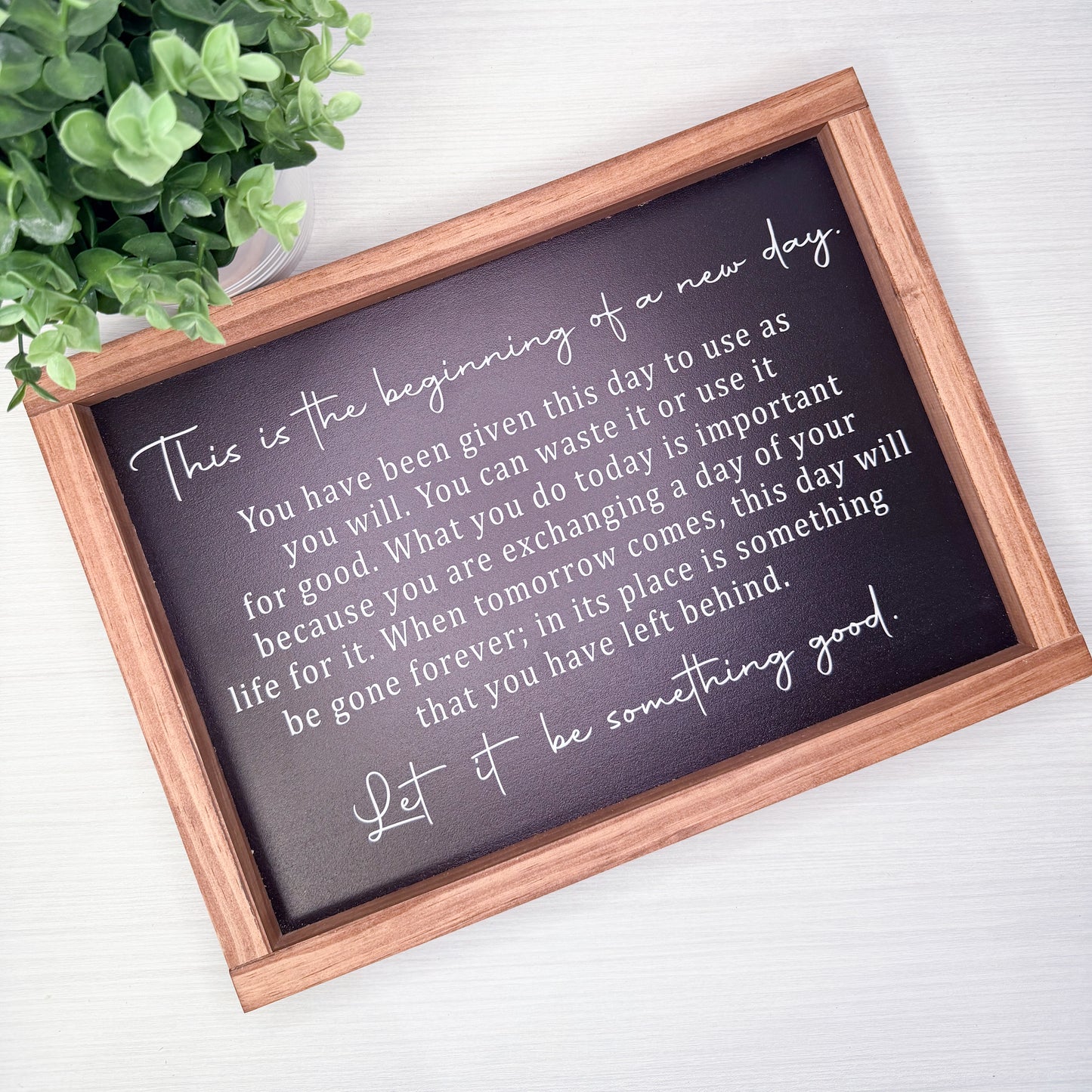 Motivational quote on a framed chalkboard with a wooden frame, placed on a light surface with a plant in the corner.