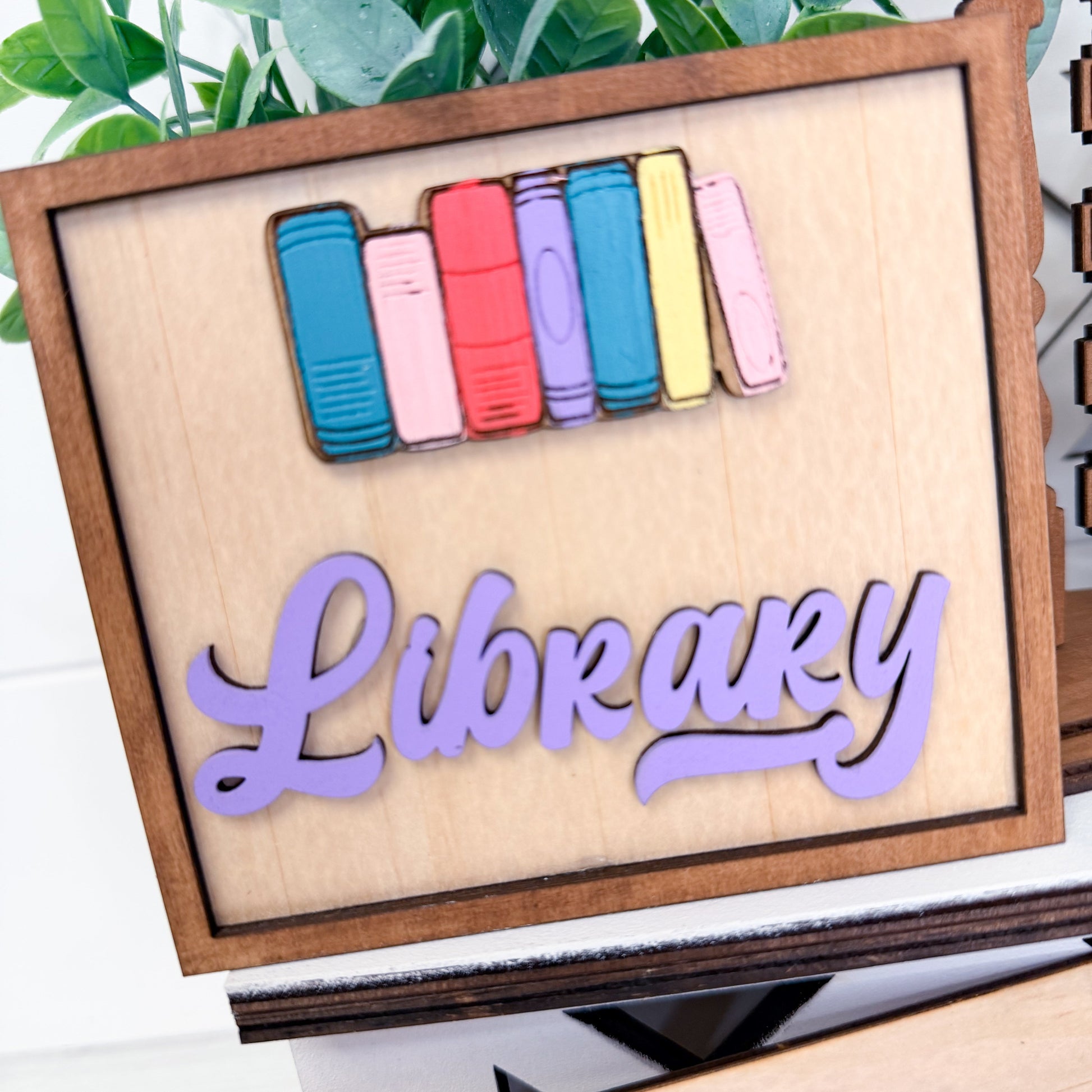 Wooden sign with colorful book-shaped decorations and 'Library' text on a white background.