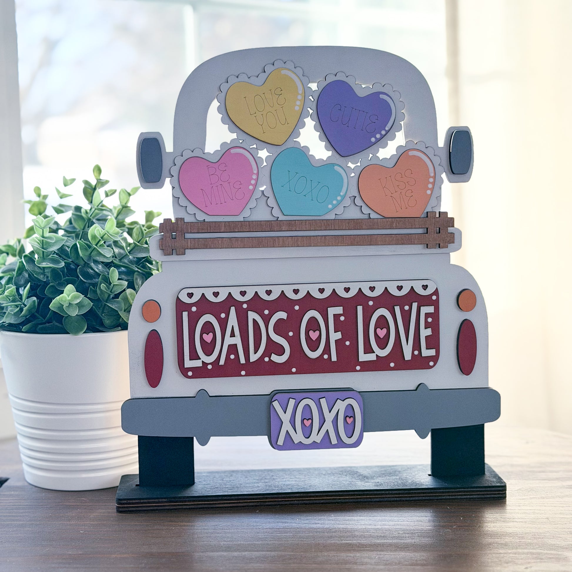 Decorative sign shaped like a truck with colorful hearts and 'LOADS OF LOVE XOXO' text on a wooden surface.