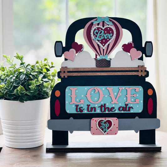 Decorative sign of a car with 'Love is in the air' text on a wooden surface.