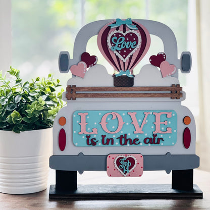 Decorative sign of a truck with 'Love is in the air' and a hot air balloon, placed indoors.