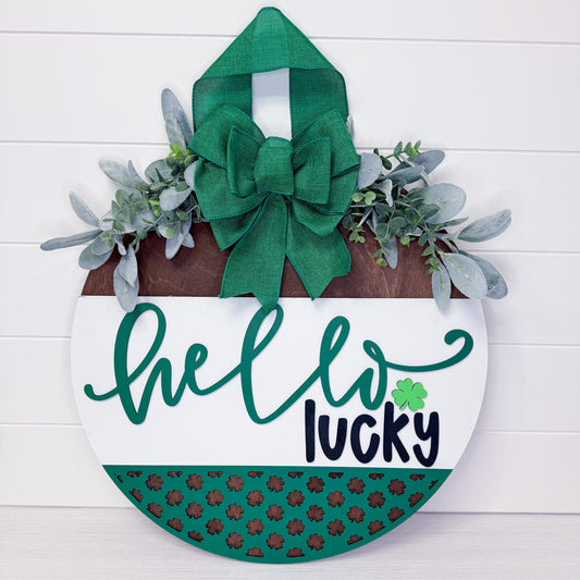 Decorative sign with 'hello lucky' text, green bow, and shamrock pattern on a white background