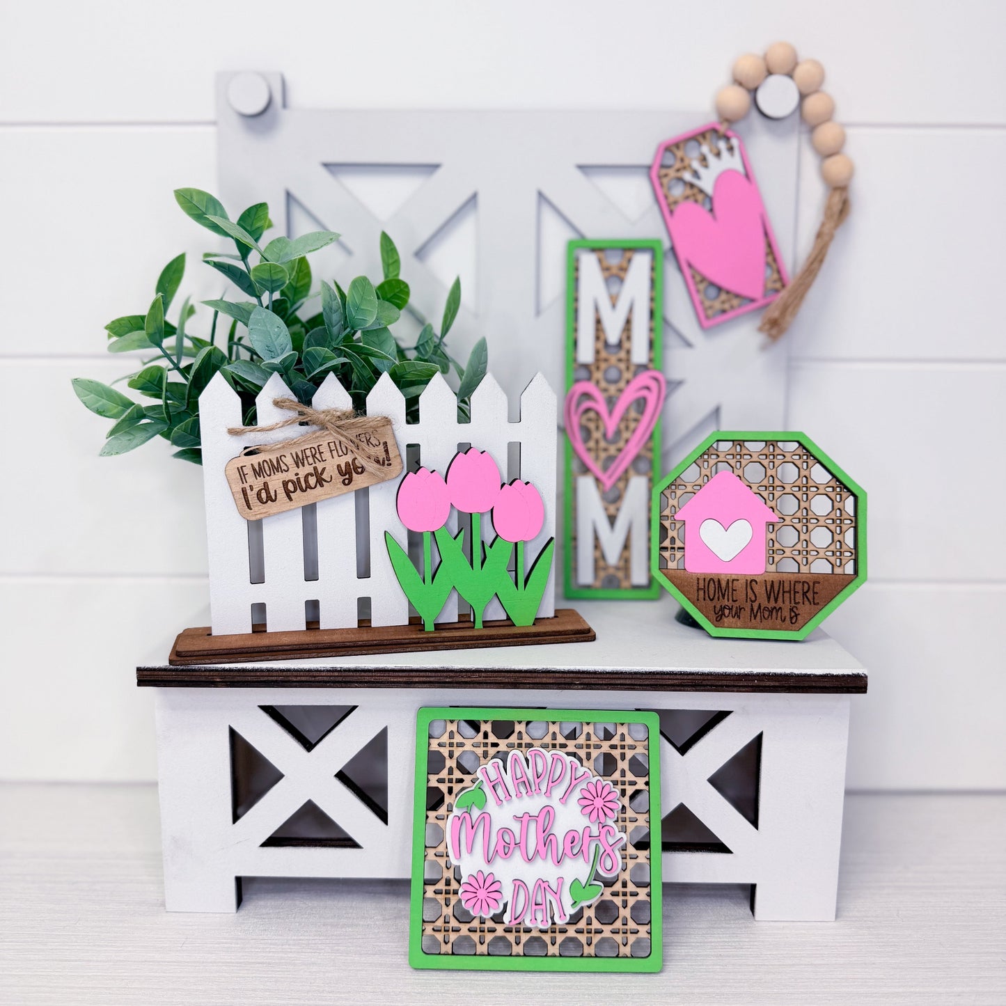 Decorative items including a small white picket fence, pink tulips, and Mother's Day-themed signs on a white surface.