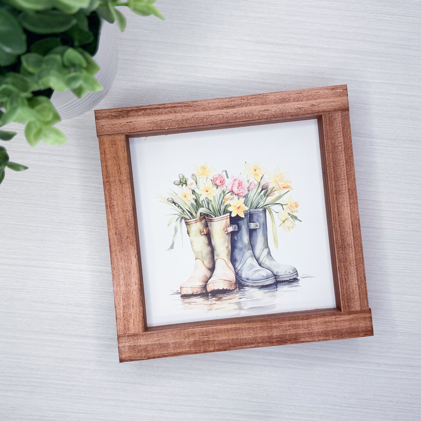 Framed artwork of rain boots with flowers on a textured wall.