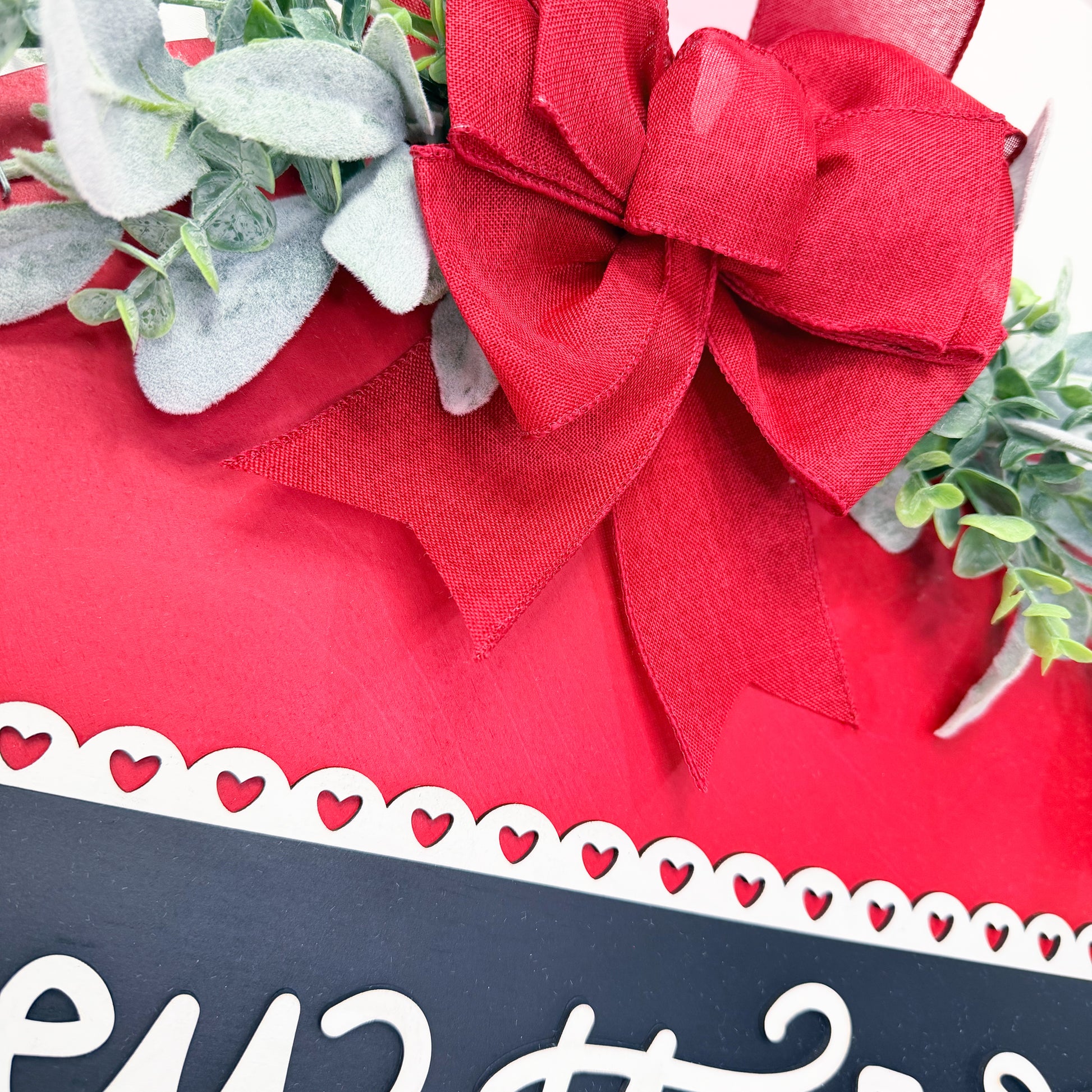 Door sign with a large red bow and greenery, featuring a decorative black and white label.