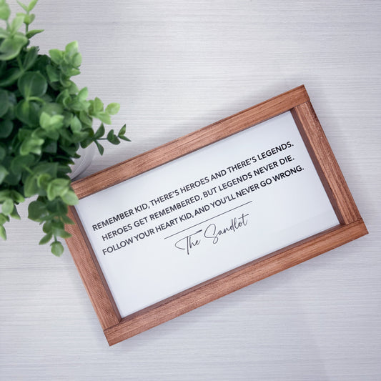 Wooden framed sign with motivational quote on a light background with a plant.