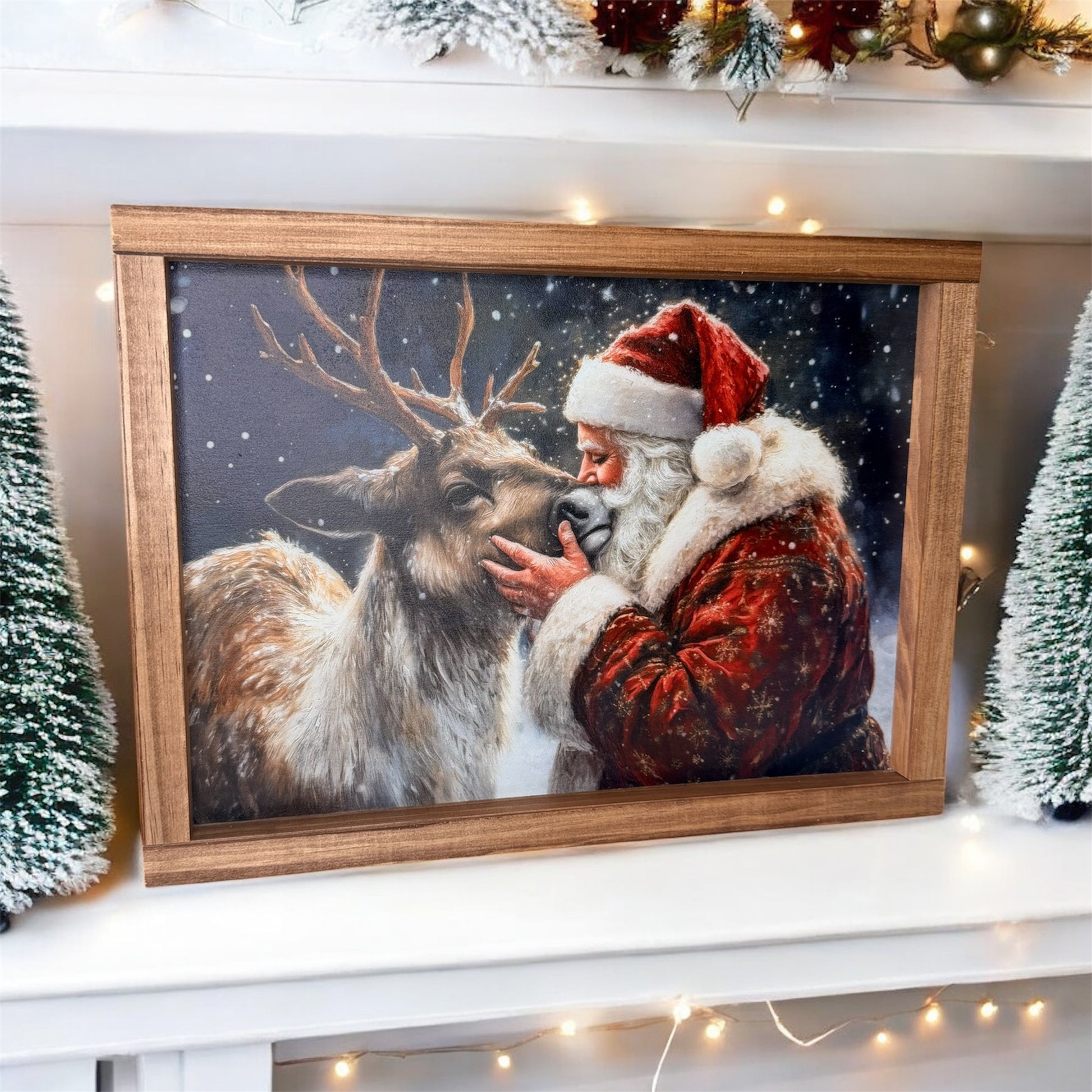 Framed picture of Santa Claus and a reindeer on a decorated shelf with Christmas lights and trees.