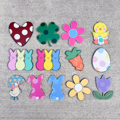 The collection includes a red and white polka dot heart, a green shamrock, a pink flower, a yellow chick, a pastel bunny trio, a carrot, a polka dot egg, a duck under an umbrella, pink and blue bunnies, a yellow flower, and a purple tulip.
