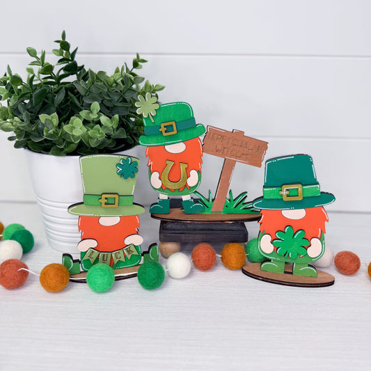 Decorative gnomes with green hats and red beards on a white surface with a plant in the background.